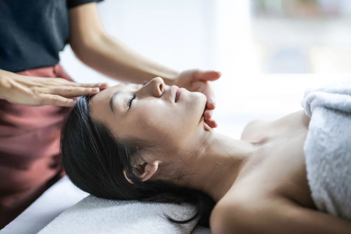 An aesthetician's hands giving a facial massage to a client lying on a treatment table
