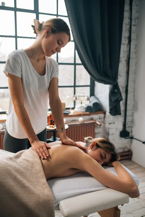 A massage therapist giving a client a back massage in a window-lit room