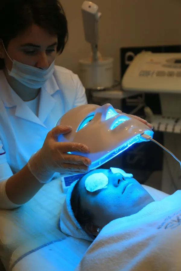 An aesthetician holding a blue LED light mask over a client's face
